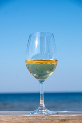 Elegant glass of white wine sits on a wooden table against a serene blue ocean backdrop, capturing a moment of relaxation and enjoyment in a coastal setting