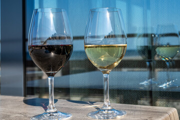 Two elegant wine glasses filled with red and white wine, placed on a wooden table, showcasing the beauty of wine selection against a bright outdoor backdrop