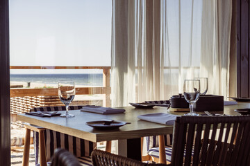 Elegant dining table set with glassware and utensils, overlooking a serene beach view through sheer curtains, creating a tranquil atmosphere for a memorable meal experience