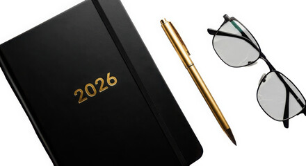 Black 2026 planner with gold lettering next to a gold pen and eyeglasses isolated on white background