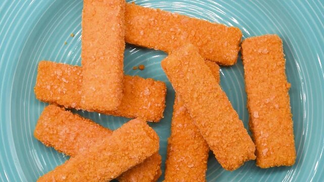 Frozen cod fish fingers rotating on a blue plate. Breaded seafood sticks ready for frying or baking, ideal for fast meals, food ads, or cooking videos.