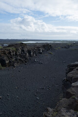 Dramatic landscape featuring rugged black volcanic rock formations, contrasting with a serene blue lake and cloudy sky, showcasing the beauty of nature's raw elements