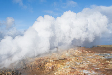 Steam rising from geothermal area with colorful mineral deposits and rocky terrain, showcasing the...