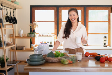 A woman stands in the kitchen, looking at the camera and smiling, preparing ingredients for breakfast.