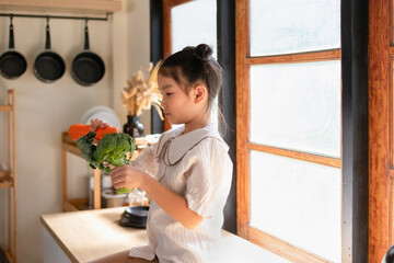 A girl sits holding vegetables in the kitchen.