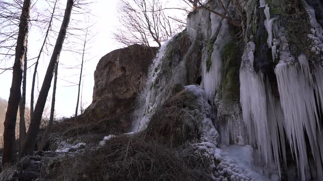 A frozen waterfall on a mountain river. The Bigar waterfall below Stara Planina is bound by ice, you can see ice stalactites and other ice forms, and some unfrozen water falling. The camera is static