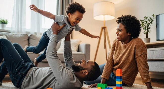 Happy black father playing with his son at home. Dad lifting laughing toddler in the air while mom watches. Joyful family bonding and parenthood concept