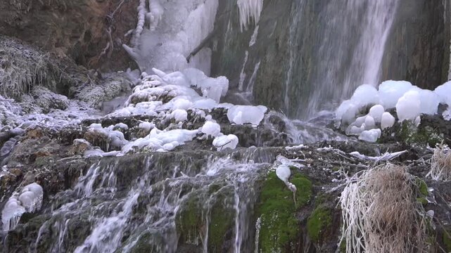 A frozen waterfall on a mountain river. The Bigar waterfall below Stara Planina is bound by ice. details of ice stalactites and other ice formations. Unfrozen falling water flows between the ice