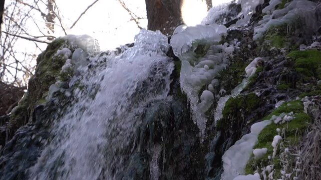 A frozen waterfall on a mountain river. The Bigar waterfall below Stara Planina is bound by ice. details of ice stalactites and other ice formations. Unfrozen falling water flows between the ice