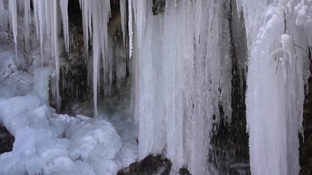 A frozen waterfall on a mountain river. The Bigar waterfall below Stara Planina is bound by ice. details of the icy stalactites around the camera moves upwards Unfrozen falling water flows between the
