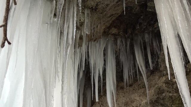 : A frozen waterfall on a mountain river. The Bigar waterfall below Stara Planina is bound by ice. details of the icy stalactites around the camera moves upwards Unfrozen falling water flows between t