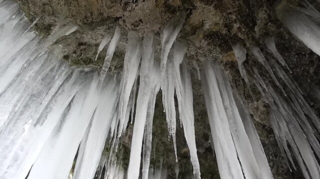 A frozen waterfall on a mountain river. The Bigar waterfall below Stara Planina is bound by ice. details of the icy stalactites around which the camera orbits. Unfrozen falling water flows between the