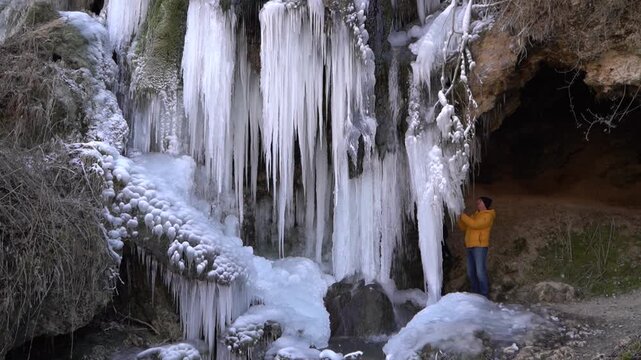 A frozen waterfall on a mountain river. The Bigar waterfall below Stara Planina is bound by ice. Unfrozen falling water flows between the ice. Tourists around the waterfall look at it