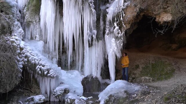 A frozen waterfall on a mountain river. The Bigar waterfall below Stara Planina is bound by ice. Unfrozen falling water flows between the ice. Tourists around the waterfall look at it