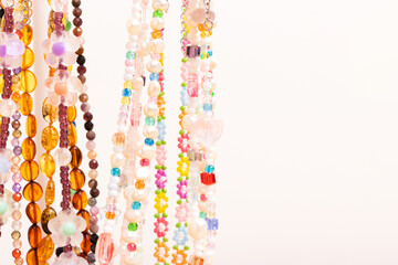 Colorful handcraft chains of beads, pearls and natural stones in front of beige background with copy space.