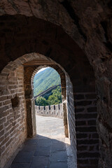 Obraz premium A restored watchtower section of the Great Wall sits prominently on a forested ridge. The steep stone staircase and the curving wall highlight the historic military architecture against clear blue sky