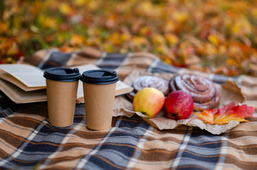 Cozy autumn picnic scene with plaid, two paper cups of hot drinks, pastries, apples and a book