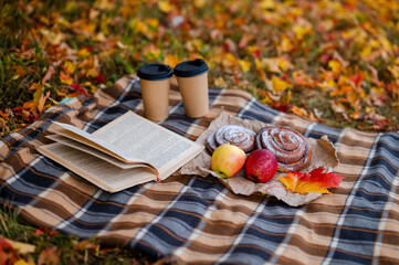 Cozy autumn picnic scene with plaid, two paper cups of hot drinks, pastries, apples and a book
