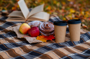 Cozy autumn picnic scene with plaid, two paper cups of hot drinks, pastries, apples and a book