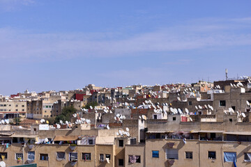 The cityscape of a Moroccan town shows rows of buildings with many satellite dishes on rooftops. This setting captures everyday life against a clear blue sky