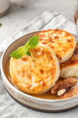 Cottage cheese pancakes or syrniki with walnuts and honey on ceramic plate on light gray kitchen table close up. Healthy sweet breakfast