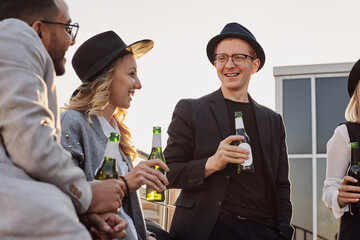 Multiethnic group of young fashionable people drinking beer, chatting and having a good time on rooftop terrace