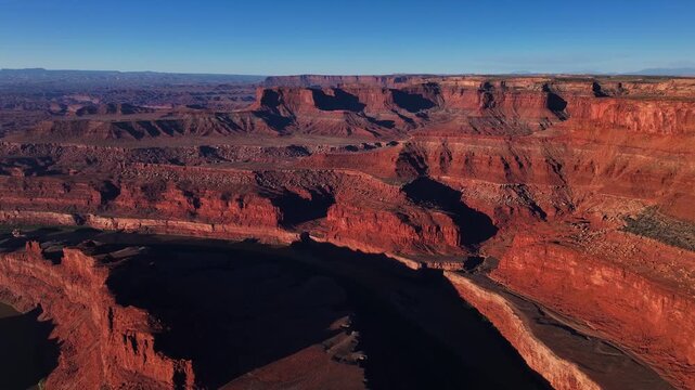 Aerial view of the red rock canyons of Canyonlands National Park bathed in warm sunlight against a clear blue sky, Moab, Utah, United States.