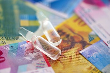 Swiss franc banknotes and medicine bottles. The current francs money bills and injection dose lies on table in big amount. The concept of medicine and vaccination in Switzerland