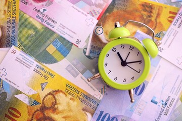 Swiss franc banknotes and alarm clock. The current francs money bills and clock lies on table in...