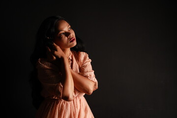 Low key portrait of a beautiful woman in a beige dress with shadows
