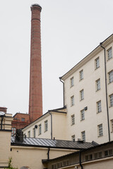 Fototapeta premium Historic brick industrial chimney and white plaster buildings in Tampere Finland representing preserved factory architecture, adaptive reuse design, and transformation of industrial heritage