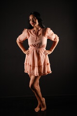 Beautiful curly dark-haired barefoot woman in a beige dress in full length on a black background