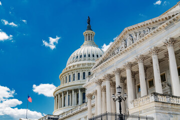 Obraz premium close-up of the Capitol dome with a fluttering American flag against a blue sky with clouds.