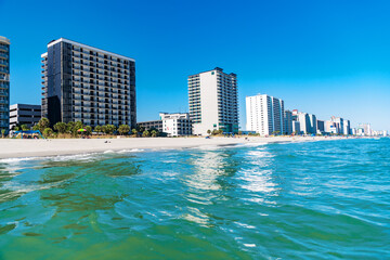 Naklejka premium Sunny beachfront with high-rise hotels and ocean waves under clear sky