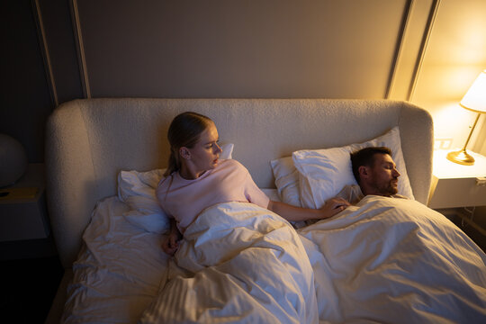 Unhappy sleep deprived woman lying awake in bed due to husband snoring in shared bedroom, insomnia. Nervous tension, female tiredness from poor sleep, restless night, disturbance and impaired sleep - Powered by Adobe