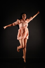 Beautiful curly dark-haired woman in a beige dress jumping on a black background