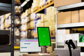 Modern storehouse facility showcases green screen on a tablet, workstation desk surrounded by...