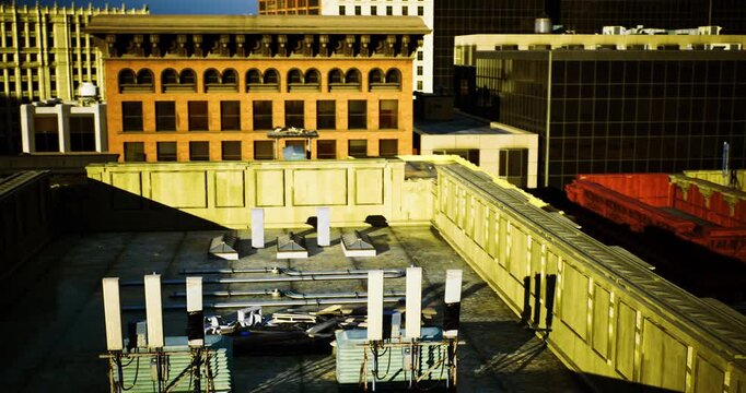 A construction site on a rooftop features materials and tools scattered across the surface. The background shows buildings of a bustling downtown area under a clear blue sky.