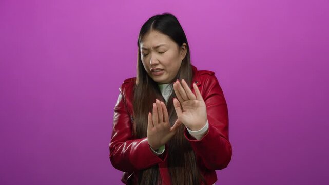 Woman in red jacket showing disgust against an isolated pink background, expressing strong aversion.