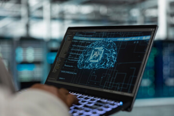 Close up of engineer using laptop in data center housing advanced infrastructure used for AI workloads. Server room IT professional running artificial intelligence code to reduce rigs latency