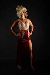 Full length portrait of beautiful woman in a red evening dress and a white wig on a black background
