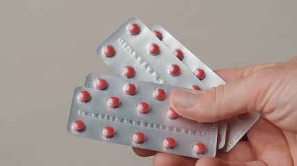 A hand shows blister packs of red pills, highlighting the importance of medication and health management - Powered by Adobe