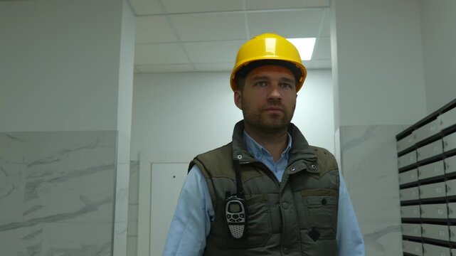 Close up portrait of Caucasian male constructor in yellow helmet walks in building taking walkie-talkie on construction site. Handsome male architecture inspector in hard hat.
