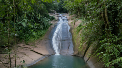 Lush greenery surrounds a cascading waterfall flowing into a tranquil, clear pool below.