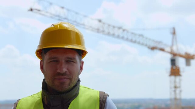Close up of handsome happy Caucasian man builder in yellow hard hat looking at camera and smiling. Young joyful male engineer in helmet with happy face at construction site