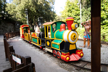 Bright, colourful childrens amusement park ride train set against greenery