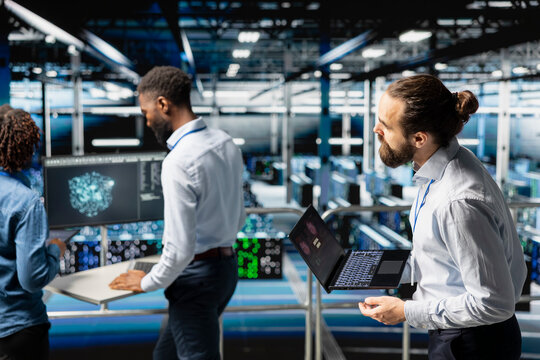 Worried technician in server room detecting hacking attempt targeting data systems and panicking about data breach. Engineering team under pressure by virus activity, emergency protocol.