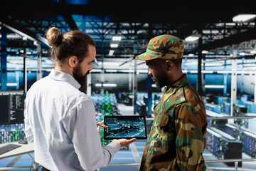 Military server room IT professionals using AI LLM tech on laptop to review network performance. Army operators managing hardware systems supporting armed forces mission for national security.