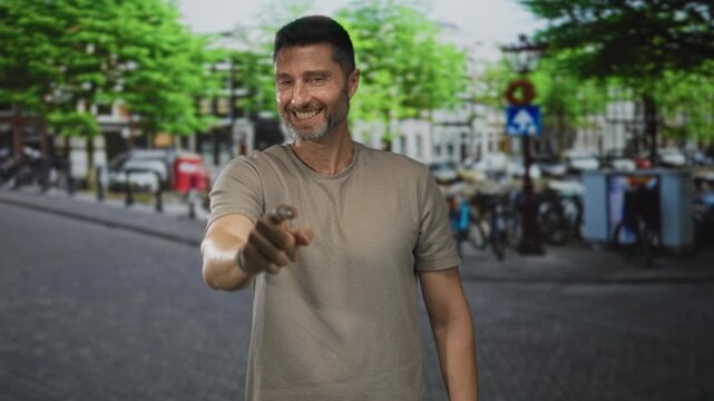 Man points finger to camera on street smiling and wearing beige tshirt; confidence connection invitation.