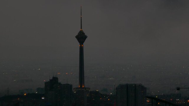 Milad Tower rises against a dark cloudy night in Tehran, its lights glowing above the cityscape, a dramatic cinematic shot blending urban life and mystery.